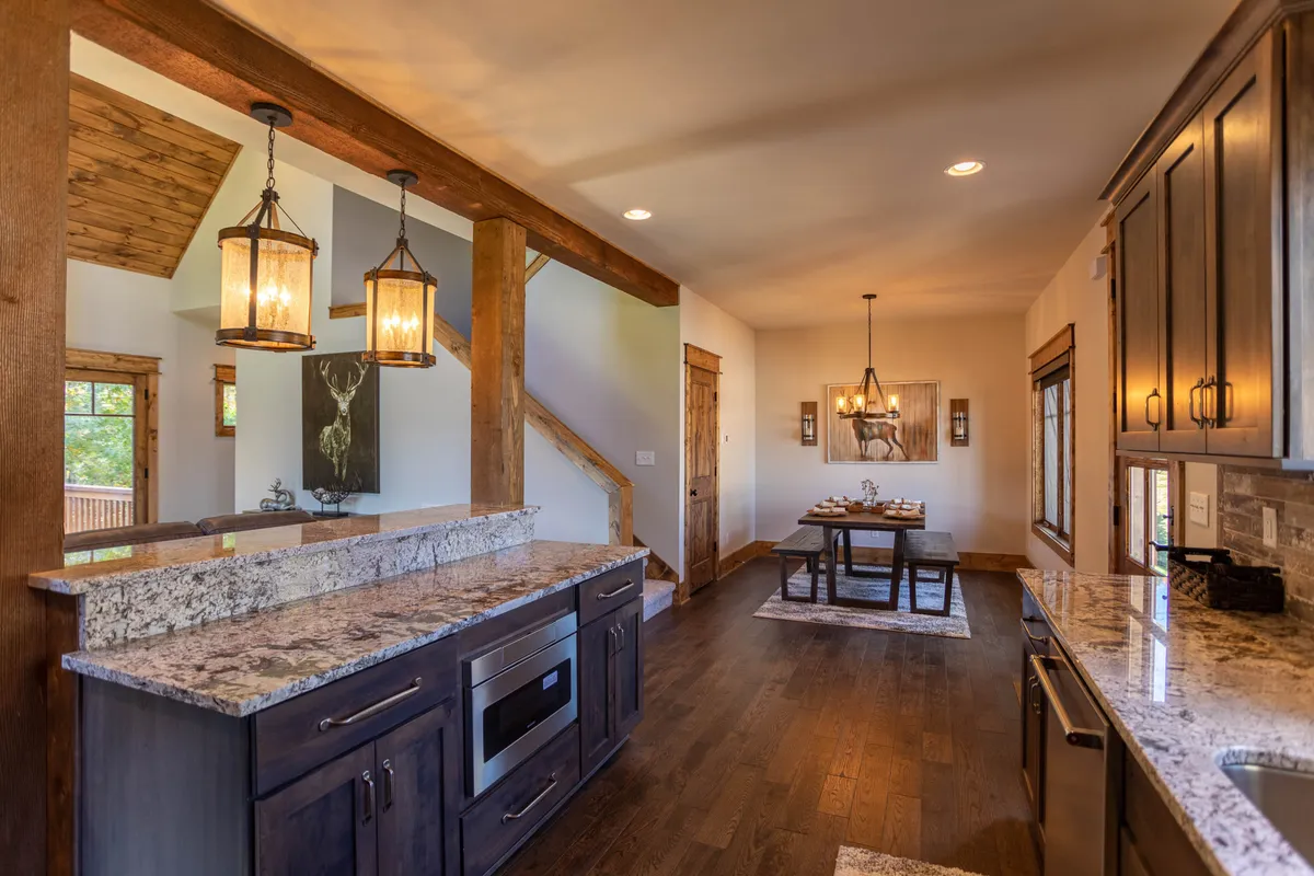 An open dining area with a large dining table surrounded by chairs, granite countertops, sturdy wooden beams, and a stylish chandelier overhead. The space feels intimate and welcoming, ideal for shared meals, family gatherings, or holiday celebrations. Art on the wall adds a personal touch.