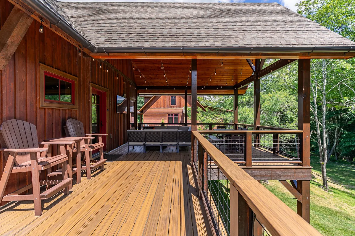 The image features a wooden deck adorned with outdoor seating, string lights, and lush greenery all around. The space exudes a welcoming, intimate vibe, perfect for socializing or relaxing in nature. The deck is oriented to capture sunset views and is suitable for morning coffee, evening gatherings, or stargazing under twinkling lights.