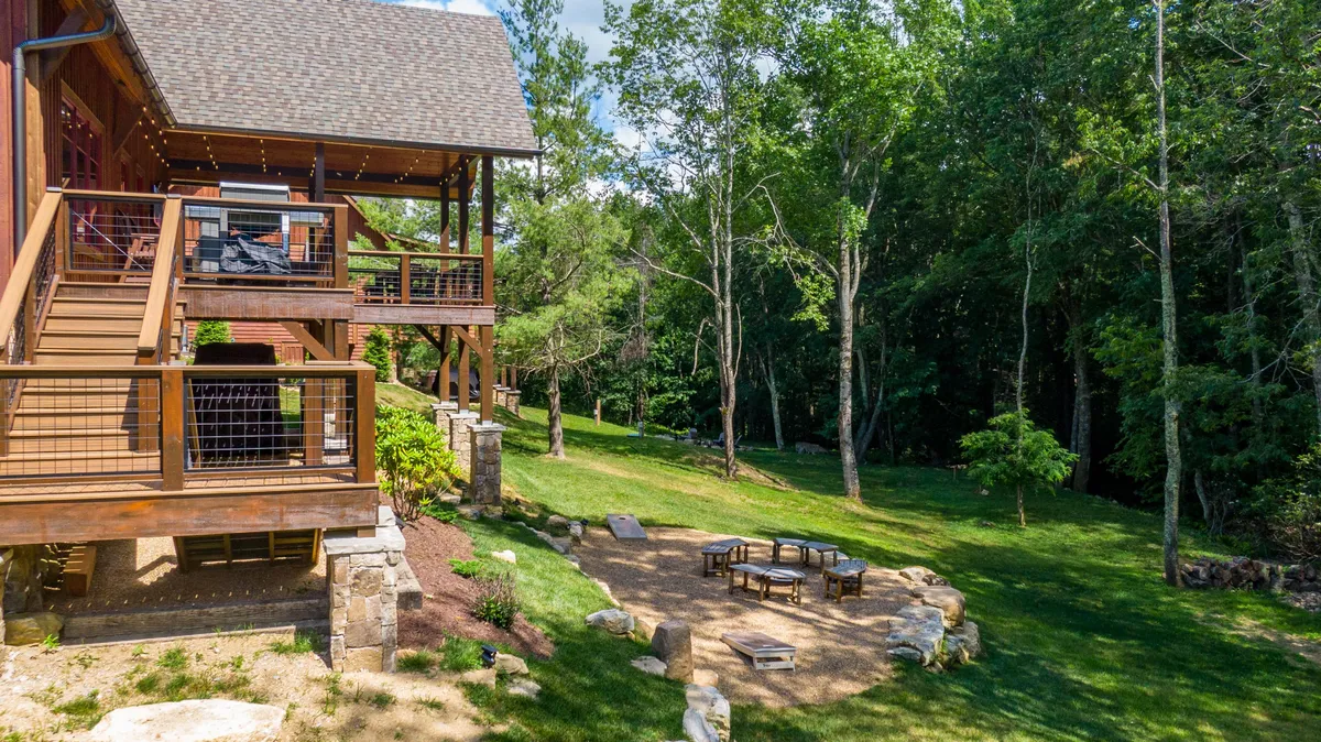 A spacious deck with seating overlooks a lush green lawn, with a dedicated fire pit area nearby. The scene invites outdoor dining, campfire gatherings, and peaceful relaxation in a natural mountain setting.