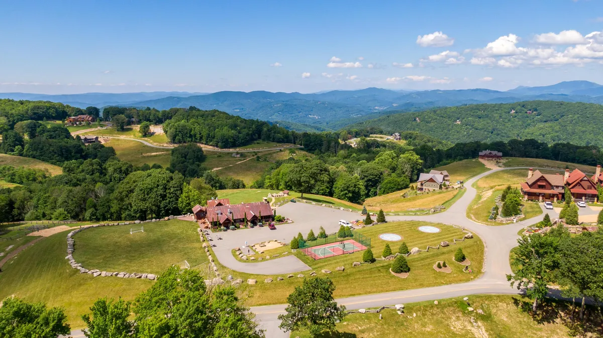 An inviting view of spacious grounds with a basketball court, lush gardens, and scenic mountains as a backdrop. Several houses are visible, and families are engaged in outdoor sports, casual gatherings, and leisurely walks, creating a peaceful yet active atmosphere.