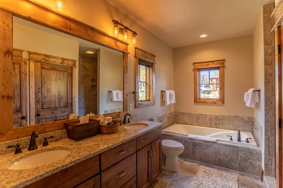 A calm, rejuvenating bathroom featuring a double sink vanity with framed mirrors, a bathtub, and a window allowing daylight to brighten the space. The setup underscores relaxation and convenience, with high-end finishes.
