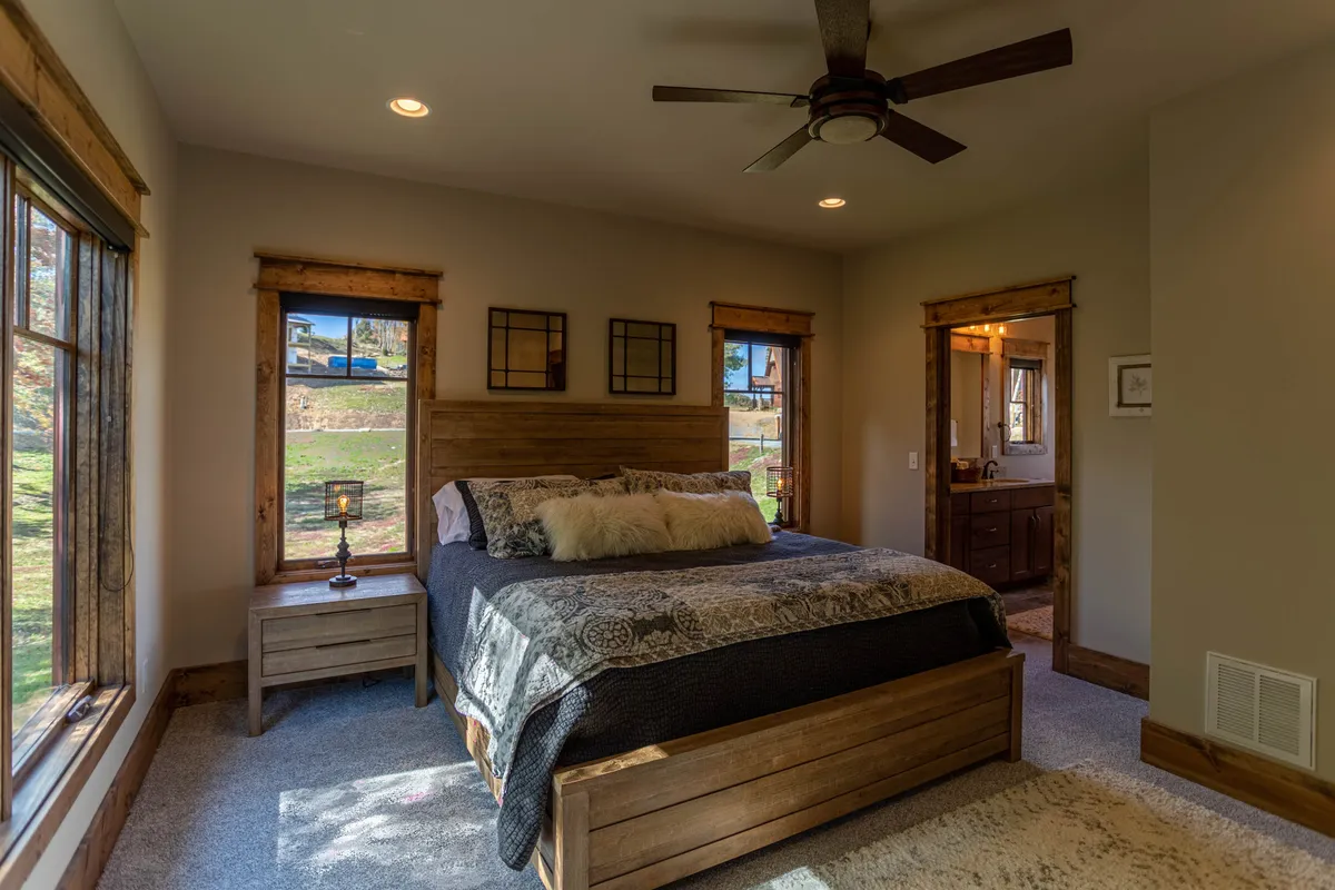 A tranquil bedroom with a comfortable bed, windows letting in natural light, a nightstand, and direct doorway access to an adjoining bathroom. The soft lighting and neutral decor create a restful atmosphere, ideal for unwinding after a day of adventure.