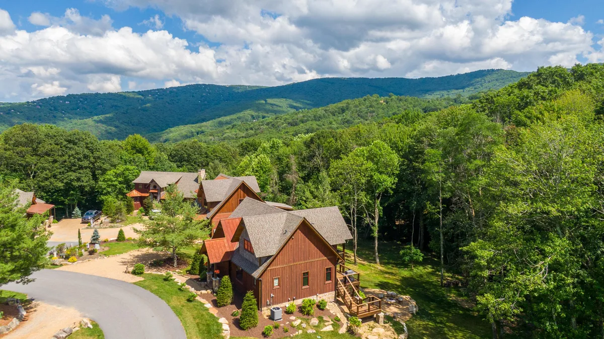 This image captures a sweeping mountain landscape with wooden cabins nestled among lush greenery and a winding road. The setting evokes a serene environment perfect for hiking, nature walks, and outdoor gatherings, all under the expansive sky.