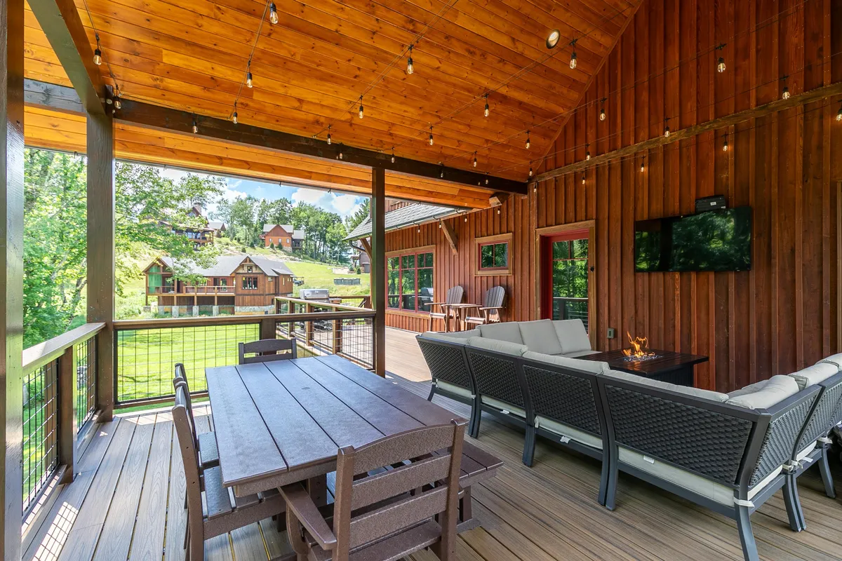 An outdoor seating area beneath a wooden ceiling, complete with a dining table set for a group and surrounded by lush green landscape. The area is designed for relaxation, outdoor meals, and socialization, with ample space for families and friends to gather, enjoy sunset views, or host barbecue parties.