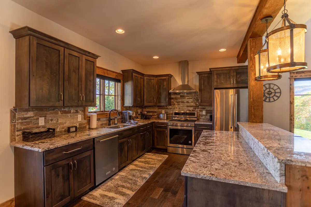 A cozy and functional kitchen with granite countertops, stainless steel appliances, ample cabinetry, a kitchen island, and a window bringing in natural light. The layout suggests an open-concept design, ideal for group meal preparation and entertaining. Visible appliances imply a fully equipped space, inviting for cooking and gathering.