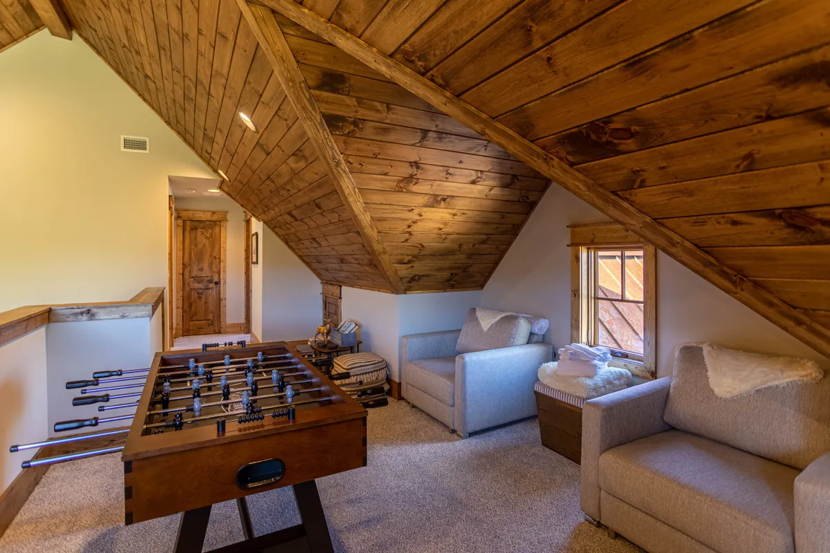 This image features a bright, airy upstairs loft with a foosball table as the focal point, surrounded by comfortable seating and wooden beams above. The scene gives a sense of casual gathering, playful competition, and a welcoming environment perfect for groups. Natural light and open space add to the inviting ambience.